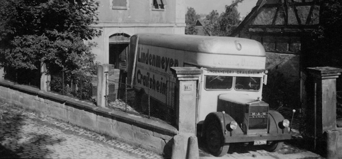 Alte schwarz-weiss-Aufnahme eines Lindenmeyer Transporters vor alten Gebaeuden